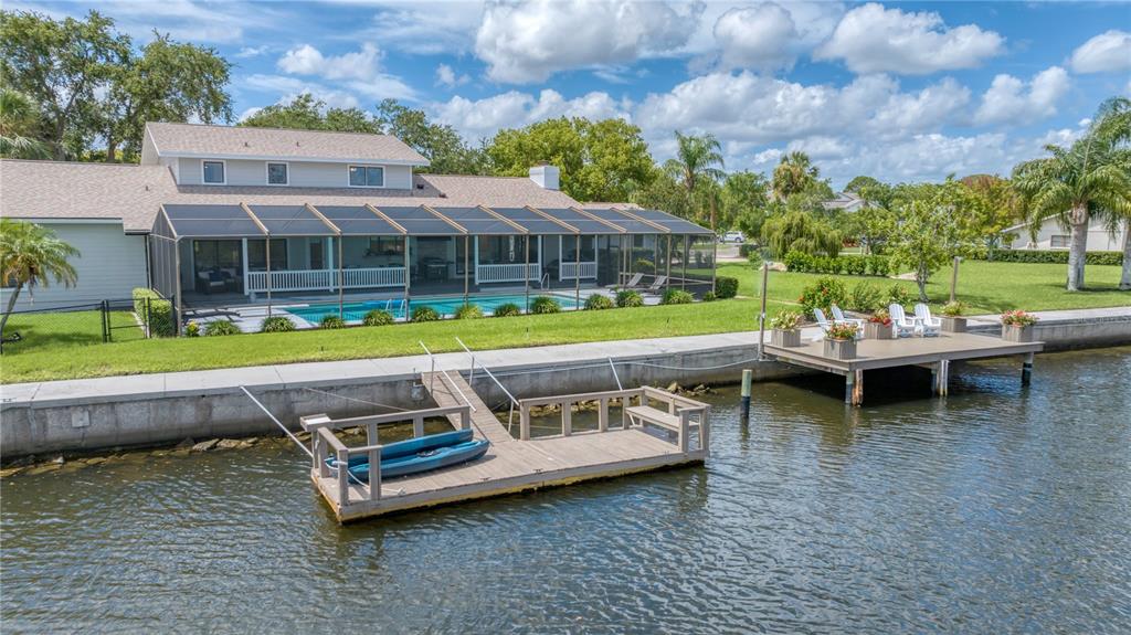A house with a screened pool enclosure sits beside a canal with a wooden dock — 5623 HULL COURT, NEW PORT RICHEY, FL