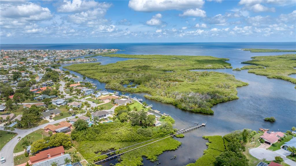 An aerial view shows waterfront houses situated near a large mangrove forest and open water — 5623 HULL COURT, NEW PORT RICHEY, FL