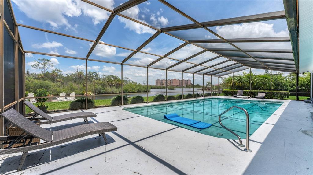 A screened-in swimming pool patio features lounge chairs and a view of a distant building — 5623 HULL COURT, NEW PORT RICHEY, FL