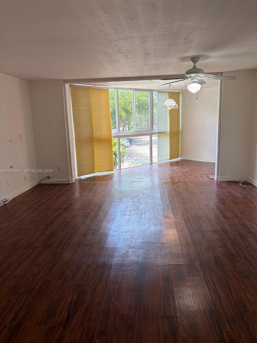 An empty room features dark wood-look flooring, a ceiling fan, and large floor-to-ceiling windows — SUNRISE, FL