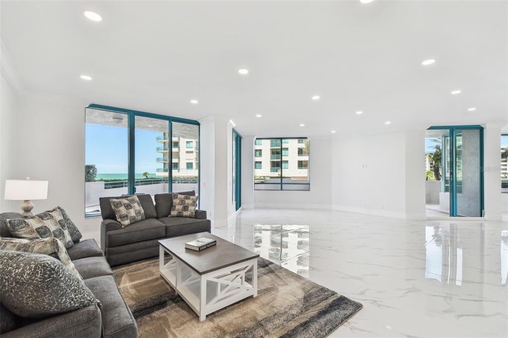 A bright living room features white marble floors, a grey sofa, and large floor-to-ceiling windows — 1560 GULF BOULEVARD UNIT 306, CLEARWATER BEACH, FL