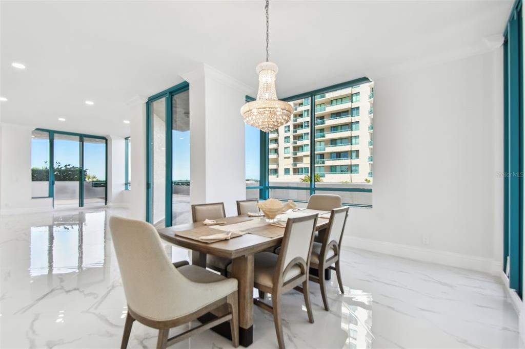 A dining room with a crystal chandelier, wooden table, and white marble floors overlooking buildings — 1560 GULF BOULEVARD UNIT 306, CLEARWATER BEACH, FL