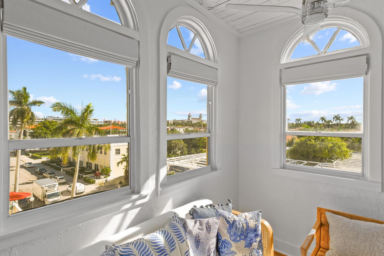 A sunroom features three arched windows overlooking a street, palm trees, and distant buildings — 235 Sunrise Avenue, Palm Beach FL 33480, PALM BEACH, FL