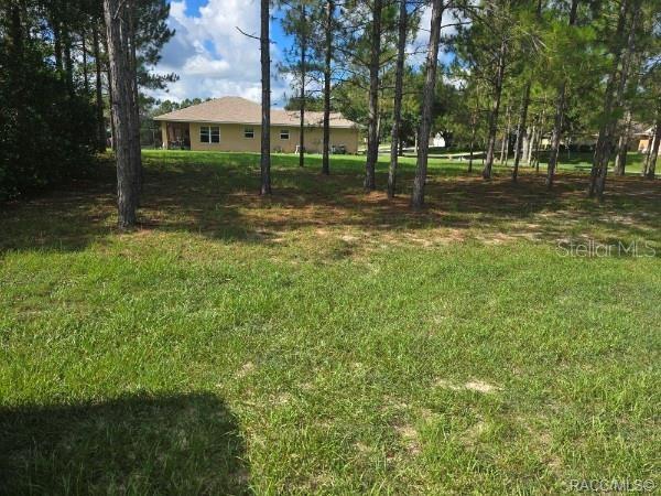 A grassy, wooded lot with a single-story house visible in the background — 2590 N BRENTWOOD CIRCLE, LECANTO, FL