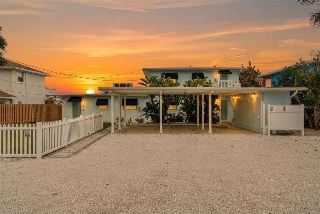 A two-story light blue house with a gravel driveway and a covered carport at sunset — 2605 BAY BOULEVARD, INDIAN ROCKS BEACH, FL