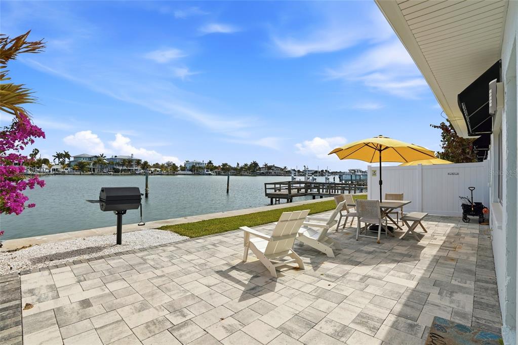 A paved patio overlooks a canal with a grill, outdoor dining set, and lounge chairs — 2605 BAY BOULEVARD, INDIAN ROCKS BEACH, FL