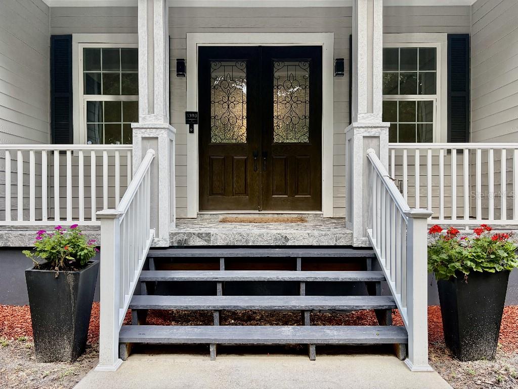 A front porch with gray steps, white railings, and a dark double door with glass inserts — 3390 WOODBERRY COURT, KISSIMMEE, FL