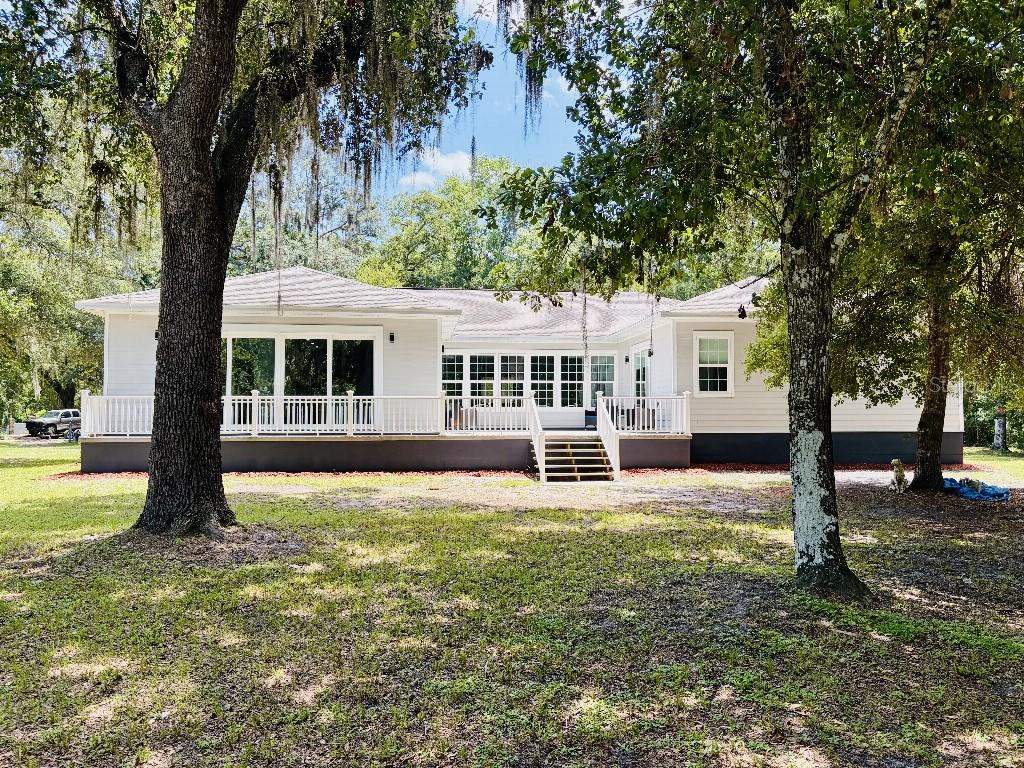 A white single-story house features a large wooden deck with white railings and mature trees — 3390 WOODBERRY COURT, KISSIMMEE, FL