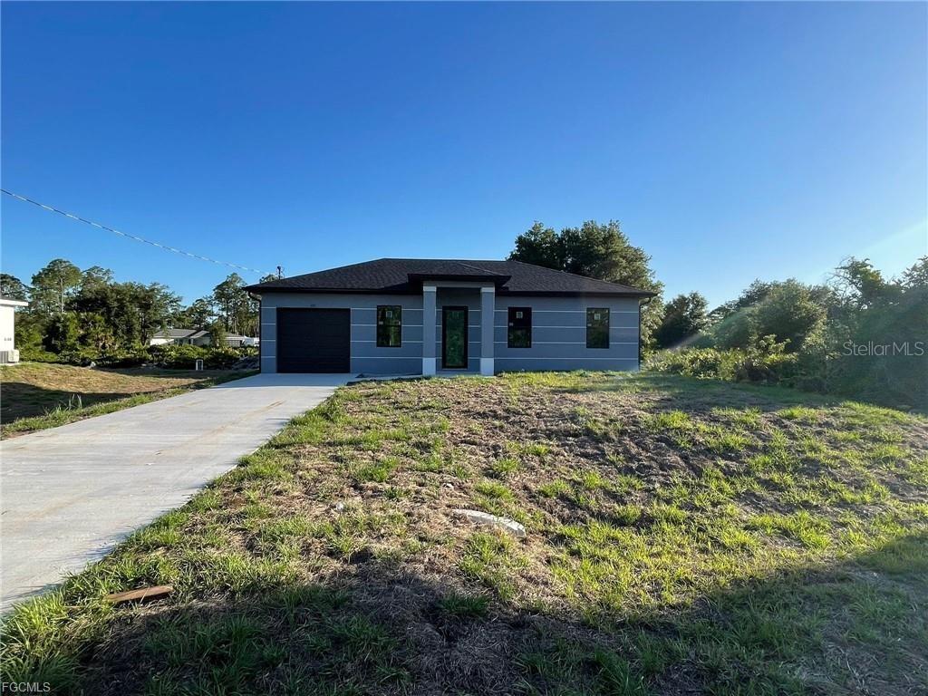 A single-story gray house with a dark roof and a concrete driveway sits on grass — 707 LEDGE STREET, LEHIGH ACRES, FL
