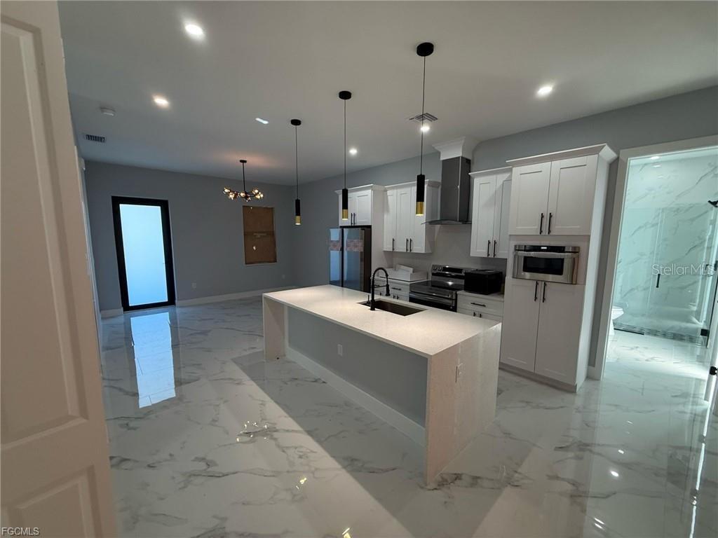 A modern kitchen features a white island, marble-look tile flooring, and white cabinetry — 707 LEDGE STREET, LEHIGH ACRES, FL