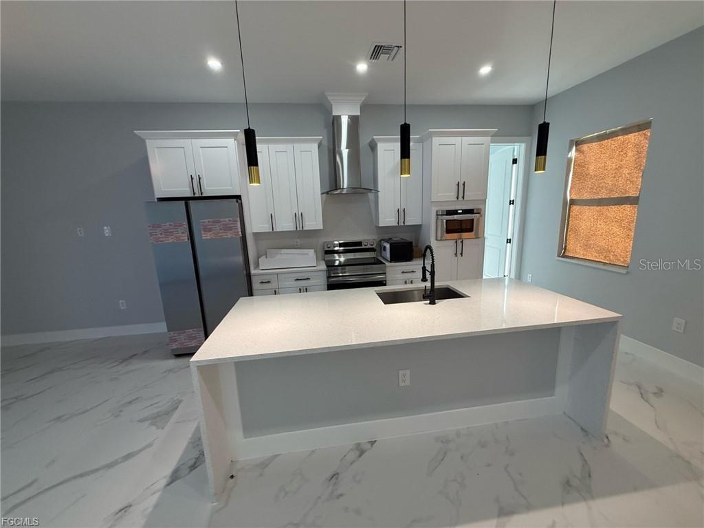 A modern kitchen features white cabinets, stainless steel appliances, and a large quartz-topped island — 707 LEDGE STREET, LEHIGH ACRES, FL