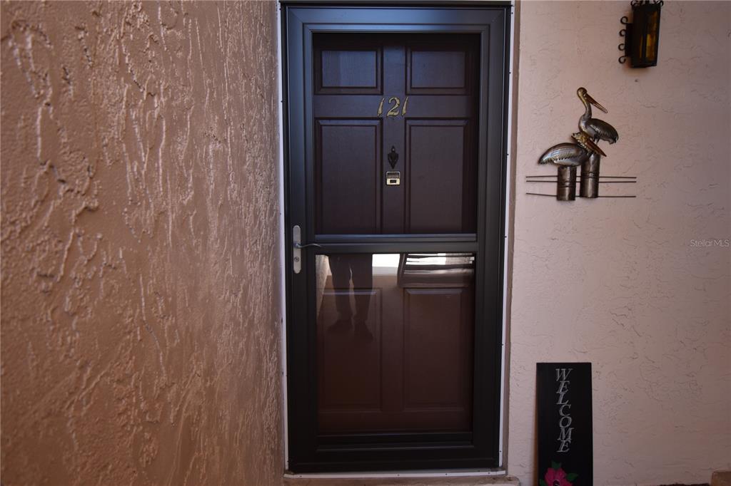 A dark brown storm door with the number 121 is mounted on a textured beige wall — 121 FERNWOOD CIRCLE UNIT 121, SEMINOLE, FL