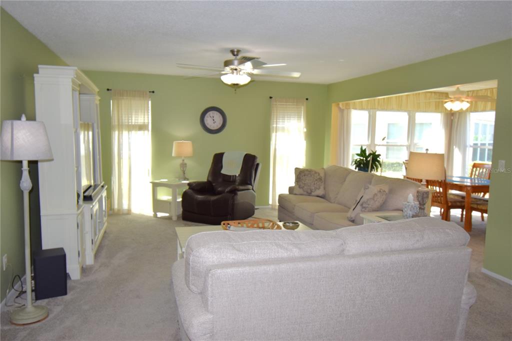 A living room with light green walls, beige carpet, a ceiling fan, and adjacent dining area — 121 FERNWOOD CIRCLE UNIT 121, SEMINOLE, FL