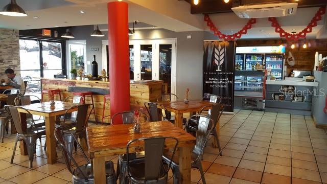 A restaurant interior features wooden tables, metal chairs, a red pillar, and a beverage display cooler — Ferrocarril St. INT. TORRES ST., PONCE, PR