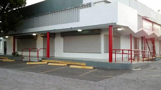 A commercial building exterior with white walls, red support columns, and closed metal security shutters — Ferrocarril St. INT. TORRES ST., PONCE, PR