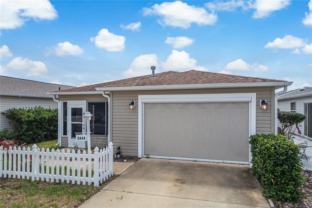 A single-story house with tan siding, a white picket fence, and a garage with a screen — 2454 SOUTHERN OAK STREET, THE VILLAGES, FL