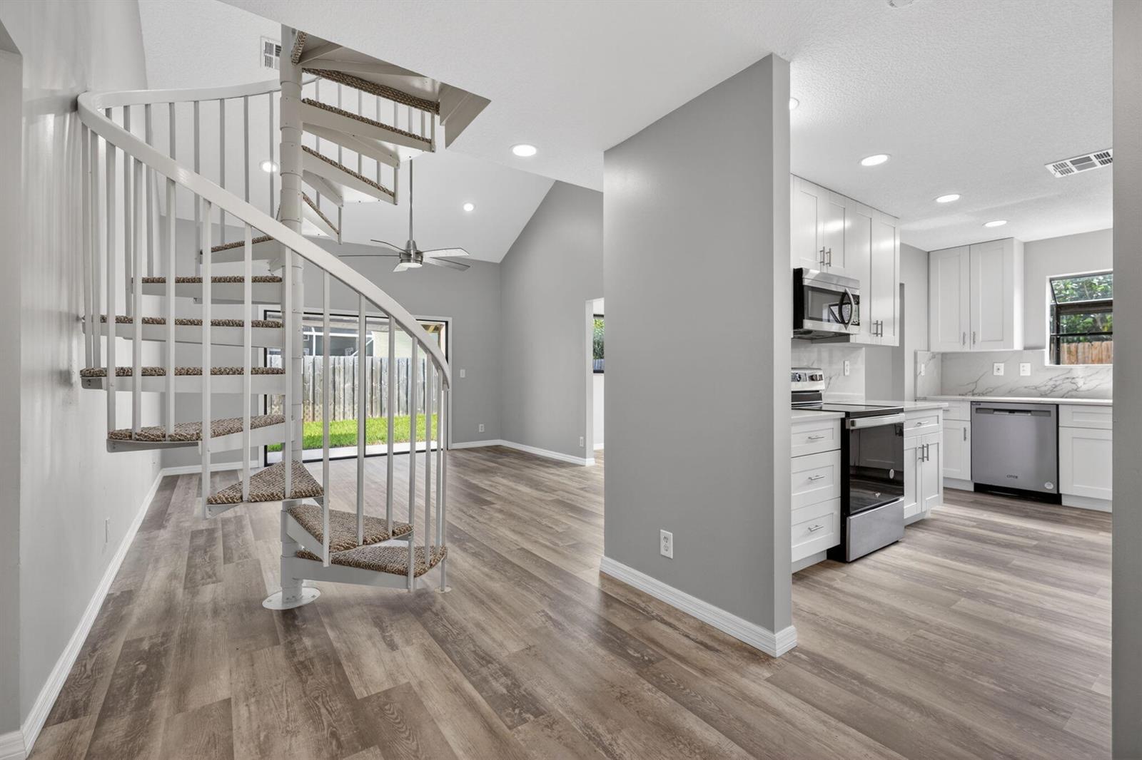 A spiral staircase stands in a living area next to a kitchen with white cabinets — 6119 Mullin Street, Jupiter FL 33458, JUPITER, FL