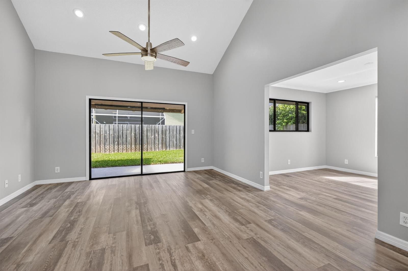 A living room with vaulted ceilings, wood-look flooring, a ceiling fan, and sliding glass doors — 6119 Mullin Street, Jupiter FL 33458, JUPITER, FL