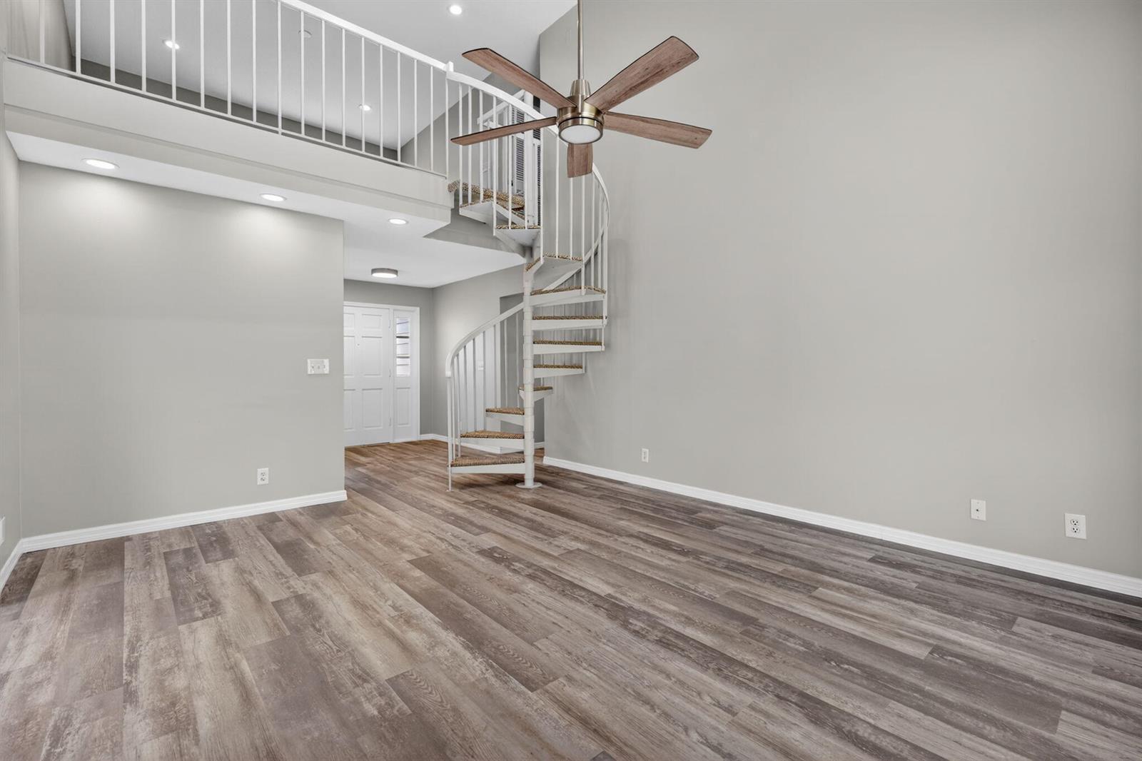 A living room with wood-look flooring, a spiral staircase, and a lofted balcony area — 6119 Mullin Street, Jupiter FL 33458, JUPITER, FL