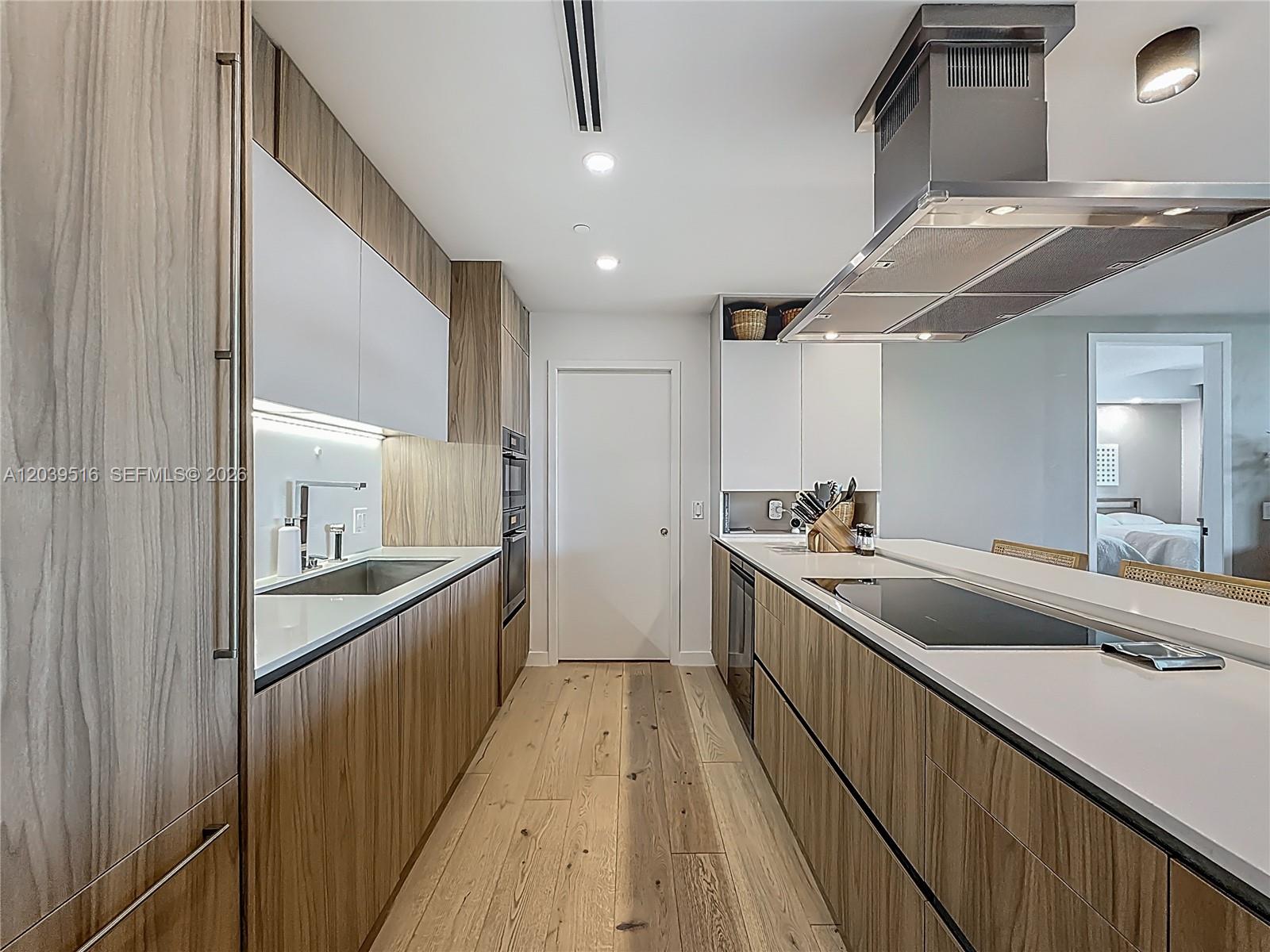 A modern galley kitchen features wood-grain cabinetry, white countertops, and stainless steel appliances — 350 Ocean Dr # 305N, Key Biscayne FL 33149, KEY BISCAYNE, FL