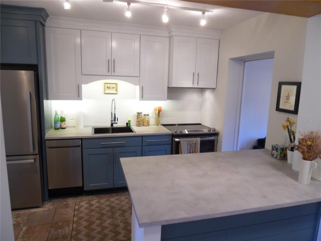 A kitchen features blue lower cabinets, white upper cabinets, stainless steel appliances, and a gray island — 5487 70TH WAY N, ST PETERSBURG, FL
