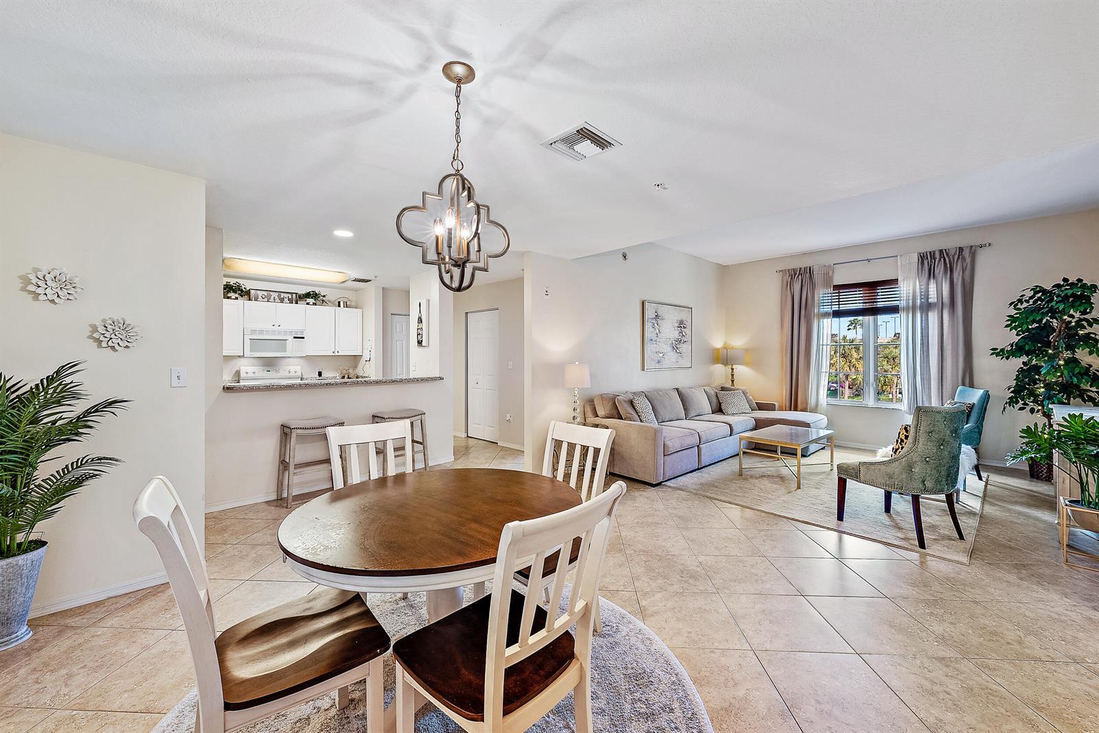 An open-concept living and dining area features tile flooring, a round table, and a kitchen — 1200 Town Center Drive # 225, Jupiter FL 33458, JUPITER, FL