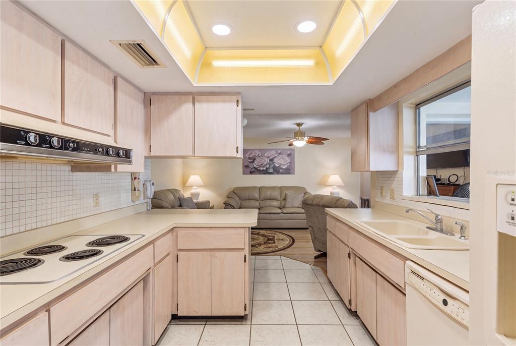A kitchen with light wood cabinets, white tile countertops, and a view into the living room — 1081 MCFARLAND STREET, DUNEDIN, FL