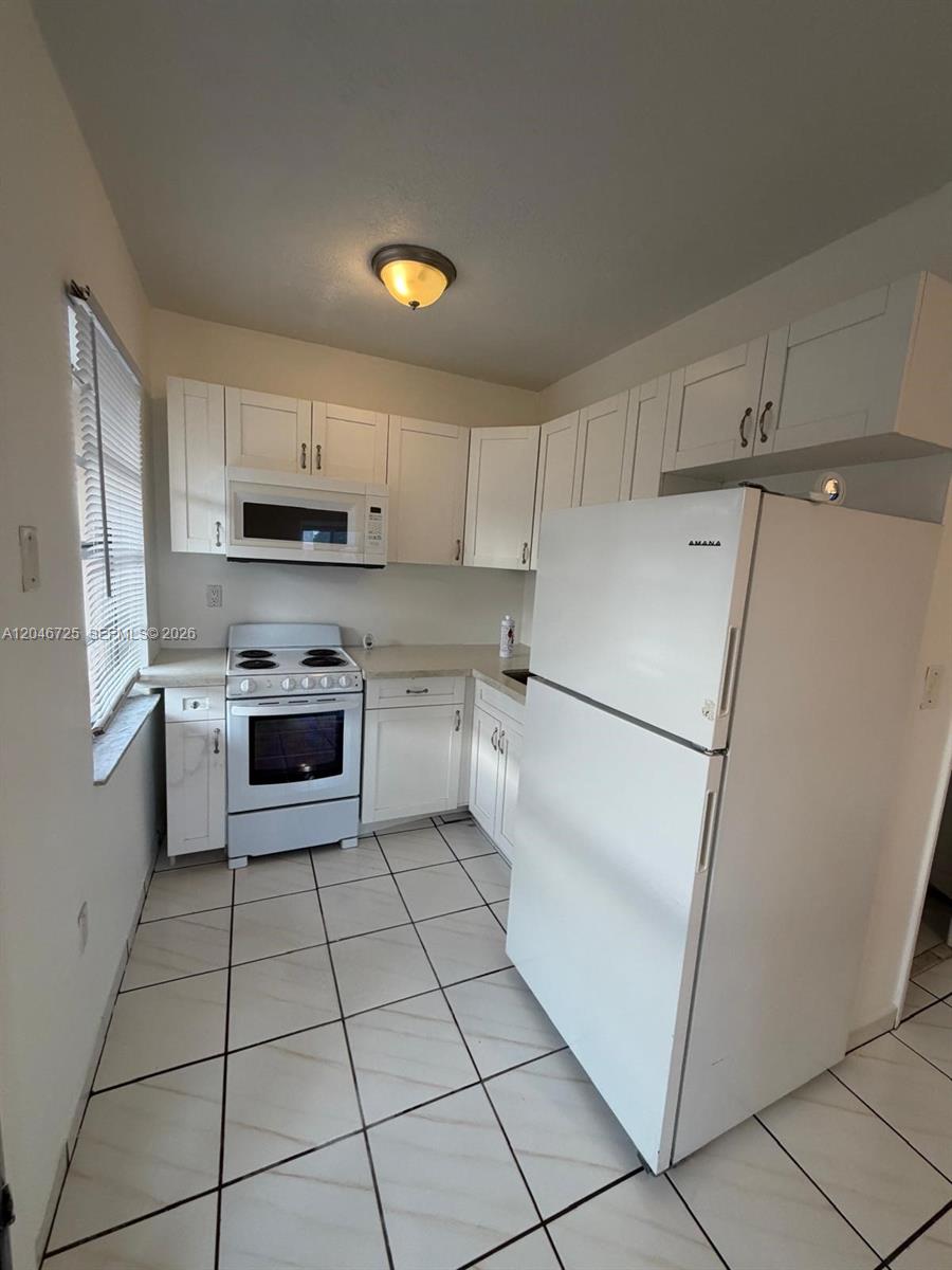 A small kitchen features white cabinets, white appliances, and light-colored tile flooring — 1036 NW 3rd St # 2, Miami FL 33128, MIAMI, FL