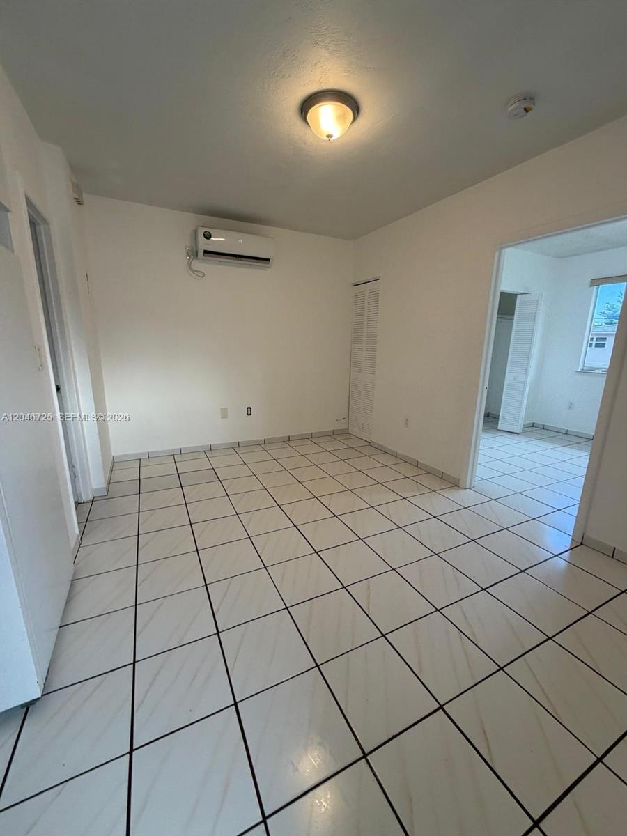 An empty room features white walls, a tiled floor, a ceiling light, and a wall-mounted air conditioner — 1036 NW 3rd St # 2, Miami FL 33128, MIAMI, FL