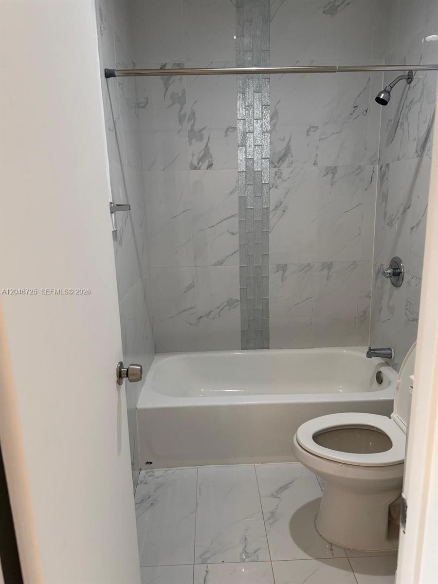 A bathroom features a white bathtub, a showerhead, and marble-style wall and floor tiles — 1036 NW 3rd St # 2, Miami FL 33128, MIAMI, FL
