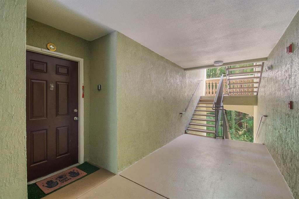 A brown front door with a welcome mat sits beside an outdoor staircase — 738 CREST PINES DRIVE UNIT 726, ORLANDO, FL