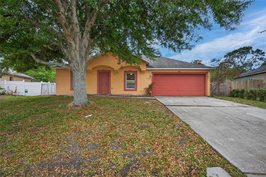 A single-story house with an orange stucco exterior, a red garage door, and a large tree — 439 MAGPIE COURT, KISSIMMEE, FL