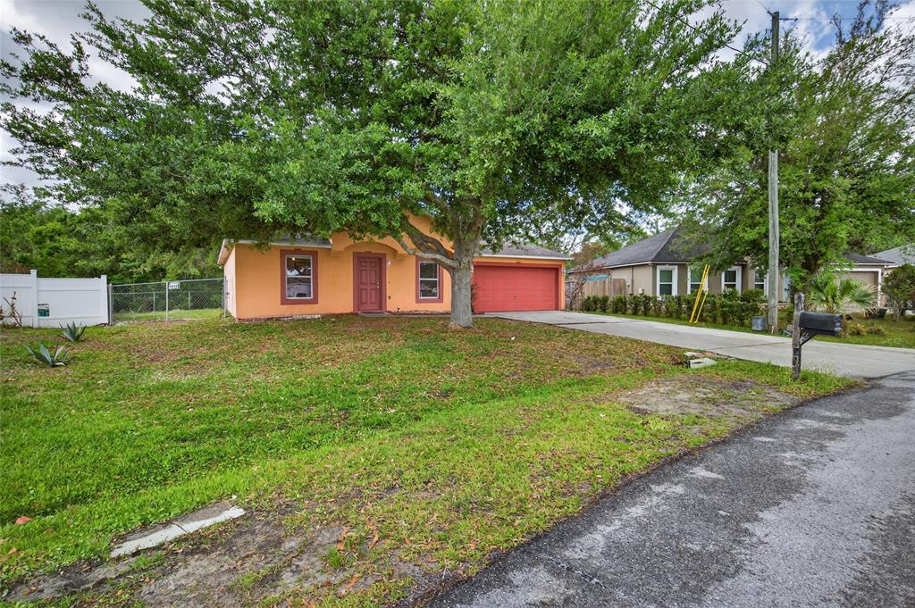 A single-story orange house with a red door and garage sits behind a large tree — 439 MAGPIE COURT, KISSIMMEE, FL