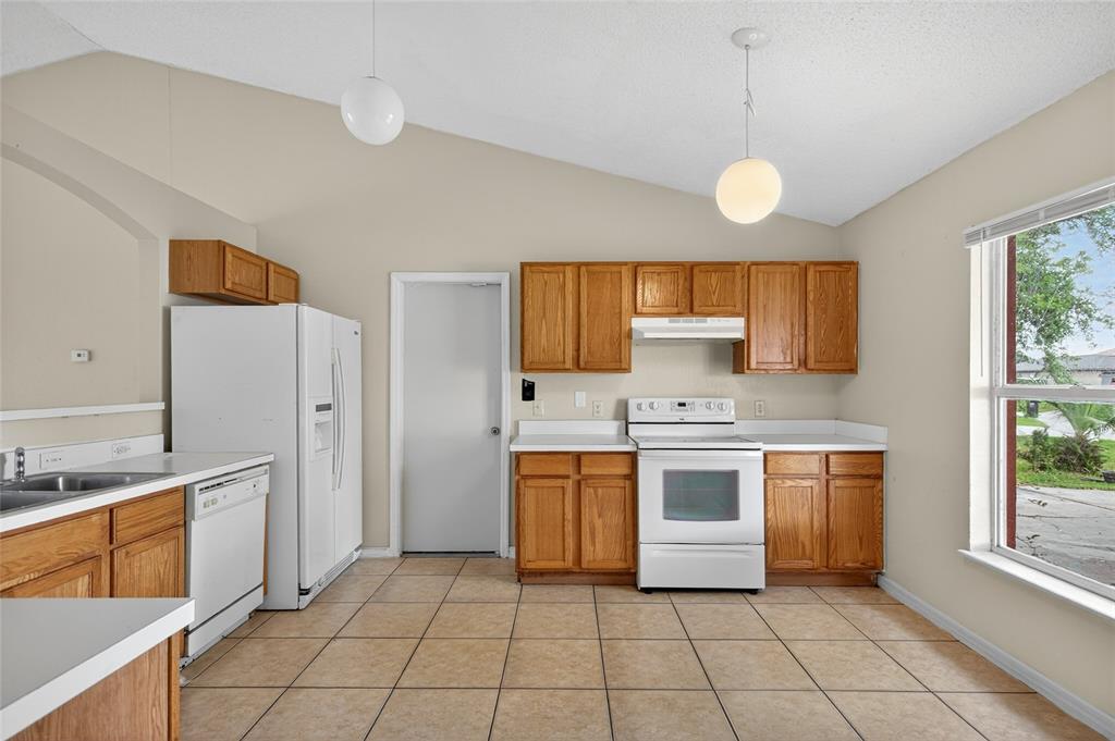 A kitchen features wood cabinets, white appliances, tile flooring, and a vaulted ceiling — 439 MAGPIE COURT, KISSIMMEE, FL