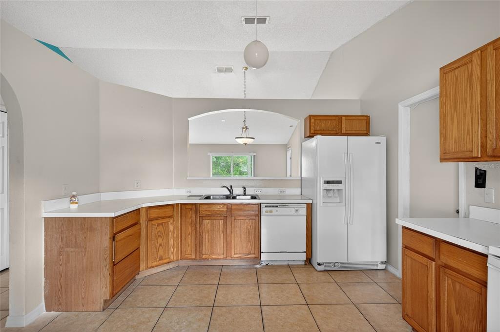 A kitchen with oak cabinets, white countertops, tile flooring, and a white refrigerator — 439 MAGPIE COURT, KISSIMMEE, FL