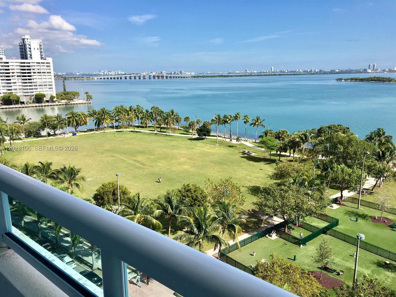 A high-angle view shows a large grassy park, palm trees, and a bay with a bridge — 1800 N Bayshore Dr # 905, Miami FL 33132, MIAMI, FL