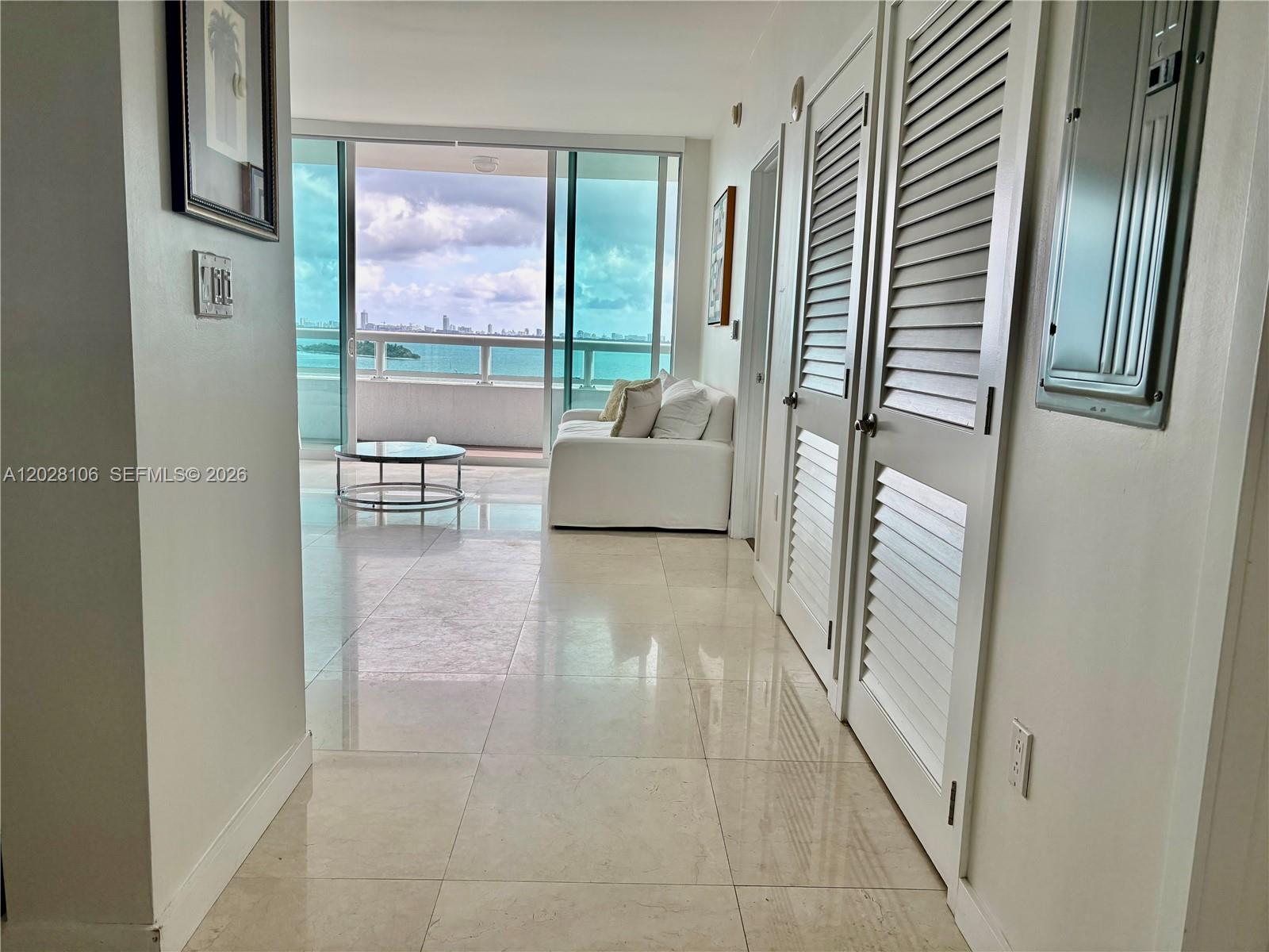 A hallway with tiled floors and louvered doors leads to a living area with balcony views — 1800 N Bayshore Dr # 905, Miami FL 33132, MIAMI, FL