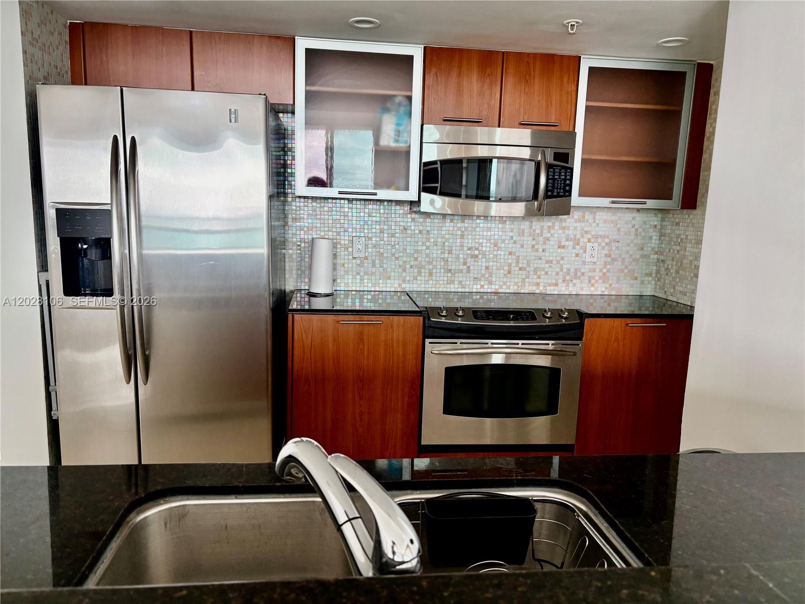 A kitchen features stainless steel appliances, wood cabinets, a mosaic tile backsplash, and dark countertops — 1800 N Bayshore Dr # 905, Miami FL 33132, MIAMI, FL