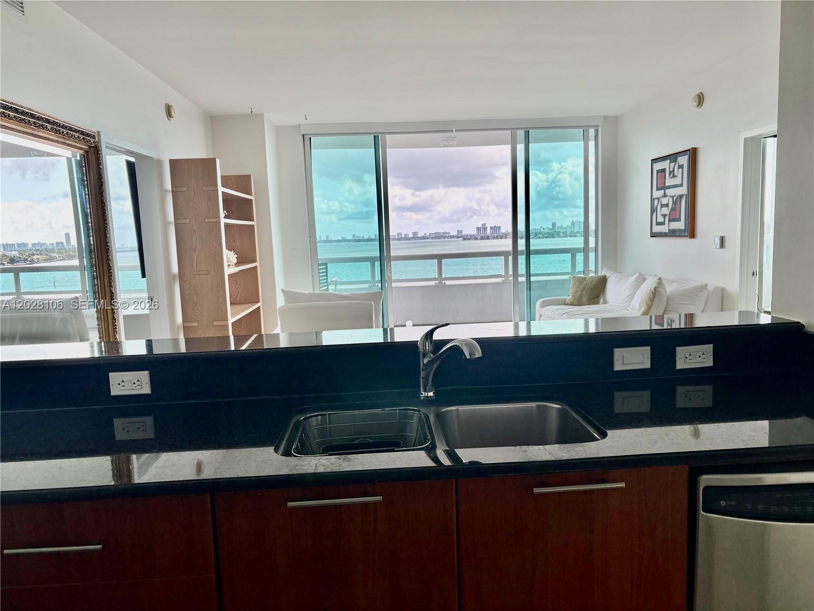 A kitchen with dark countertops and wood cabinets overlooks a living area with water views — 1800 N Bayshore Dr # 905, Miami FL 33132, MIAMI, FL