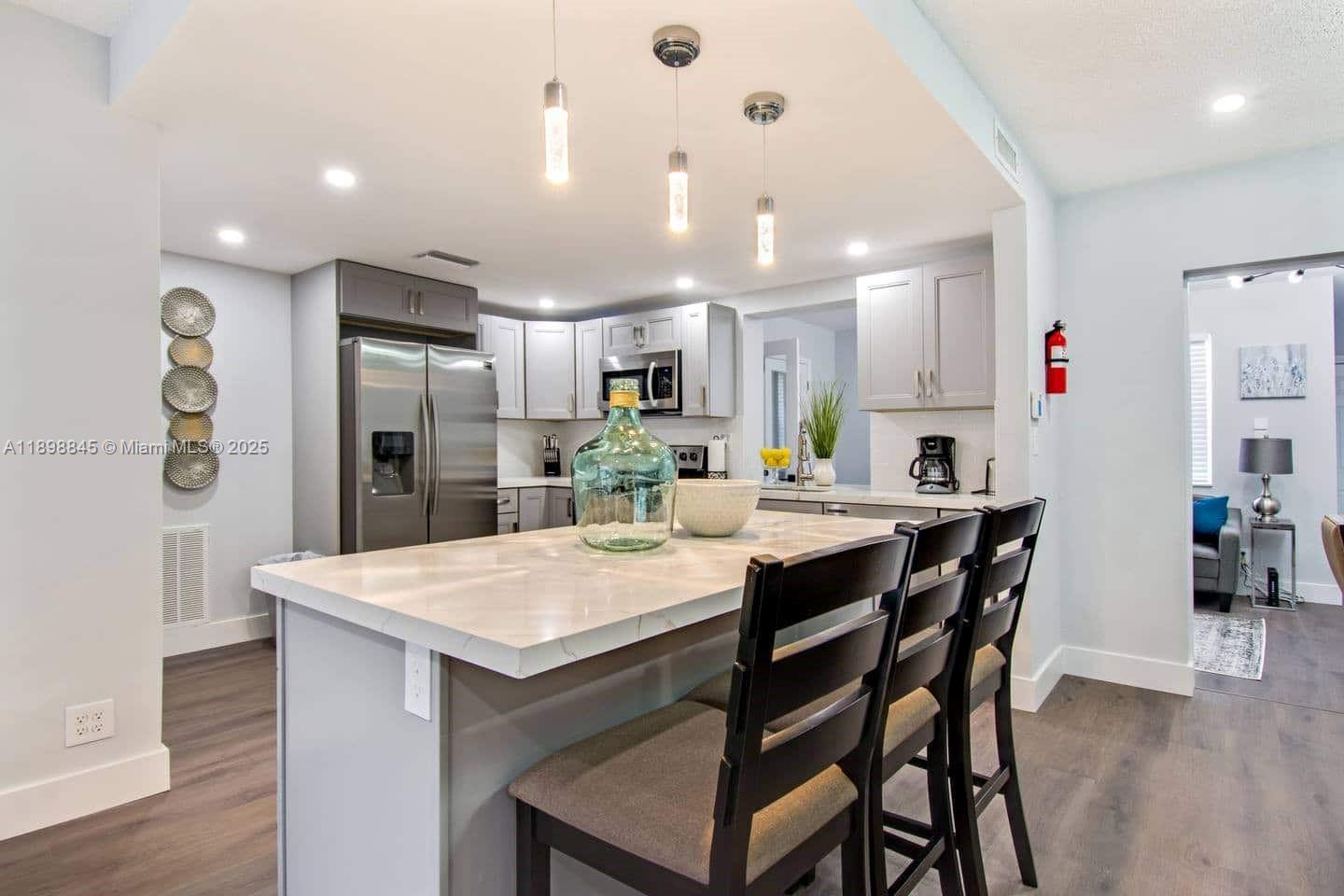 A kitchen features a white marble-topped island with three dark chairs and gray cabinetry — 1305 Funston St, Hollywood FL 33019, HOLLYWOOD, FL