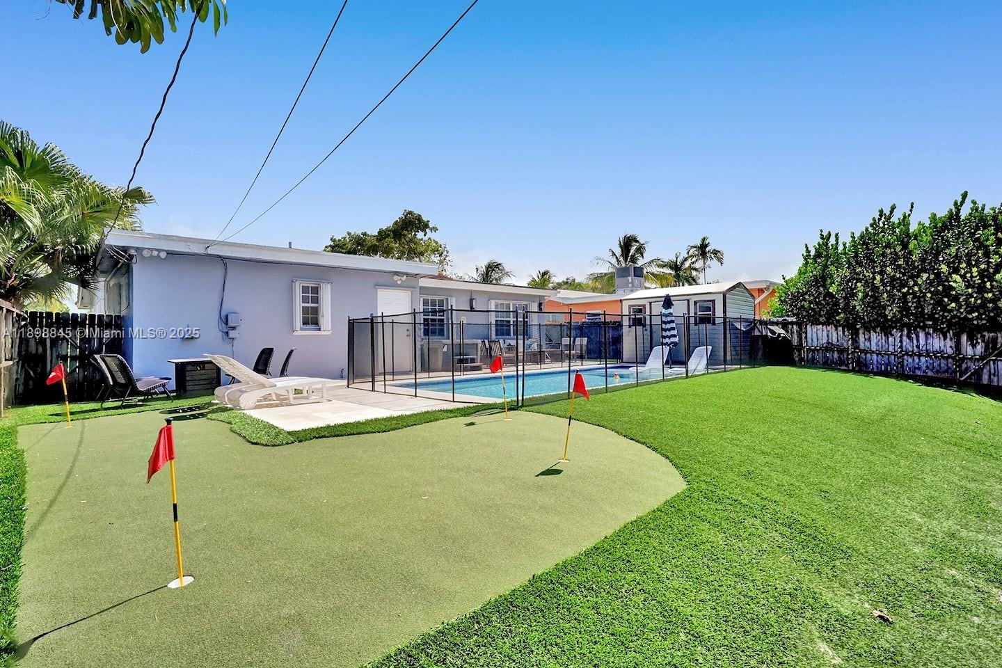 A backyard features a putting green, a swimming pool with a fence, and a house — 1305 Funston St, Hollywood FL 33019, HOLLYWOOD, FL