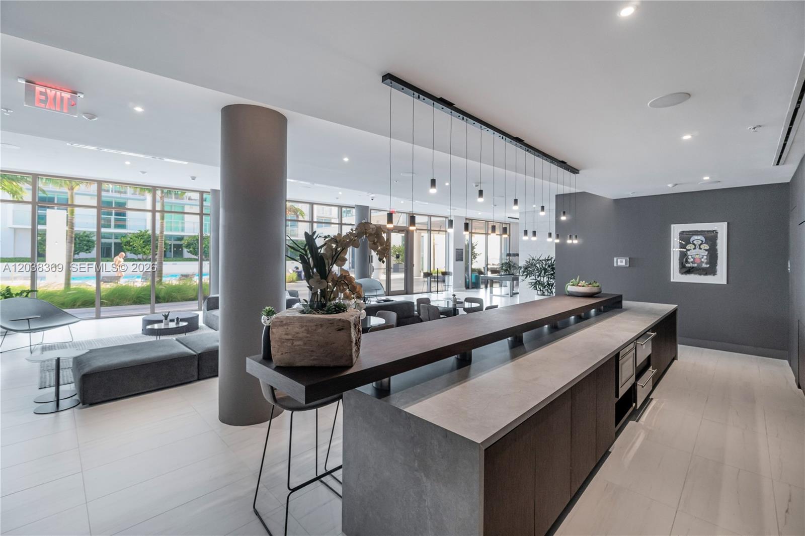 A modern kitchen island with a raised wooden bar overlooks a lounge area with floor-to-ceiling windows — 3900 Biscayne Blvd # 418, Miami FL 33137, MIAMI, FL