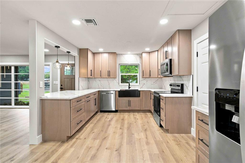 A modern kitchen features light wood cabinets, white marble countertops, and stainless steel appliances — 2770 WOOD STREET, SARASOTA, FL
