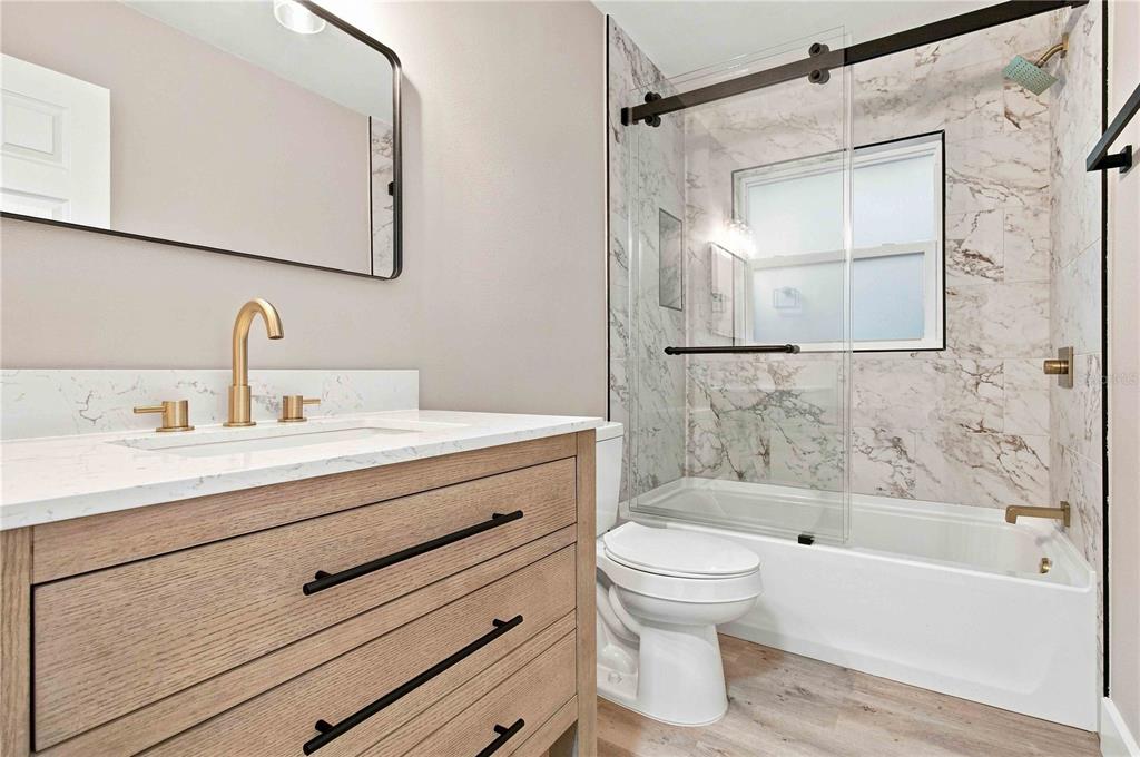 A bathroom features a wood vanity, marble-look tile shower, and a toilet — 2770 WOOD STREET, SARASOTA, FL