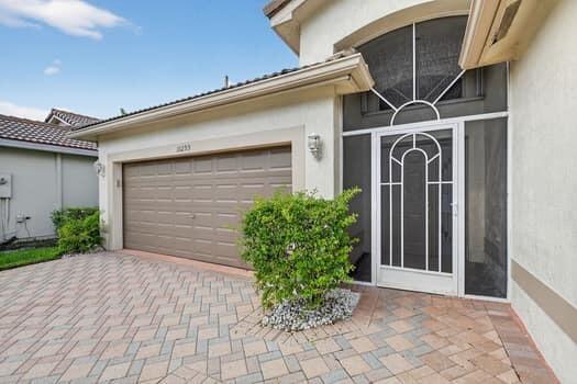 A house exterior featuring a paved driveway, a two-car garage, and a white front door — 10299 Utopia Circle W, Boynton Beach FL 33437, BOYNTON BEACH, FL