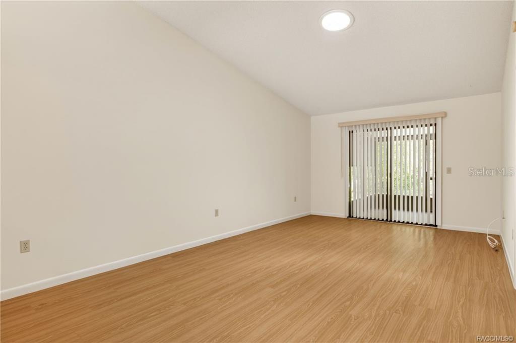 An empty room with light wood-look flooring, white walls, and a sliding glass door — 1846 JUNEBERRY LANE, INVERNESS, FL