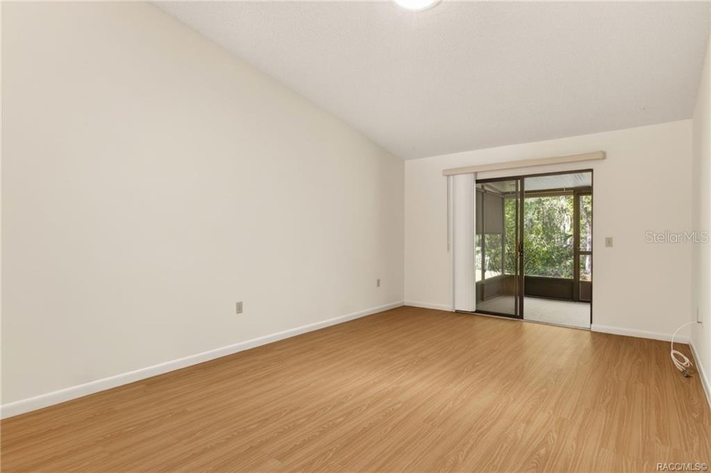 An empty room with light wood-look flooring and sliding glass doors leading to a porch — 1846 JUNEBERRY LANE, INVERNESS, FL