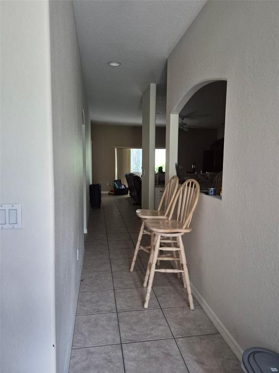 A hallway with tile flooring leads to a living area featuring two wooden bar stools — 3163 FOREST CREEK DRIVE, MELBOURNE, FL