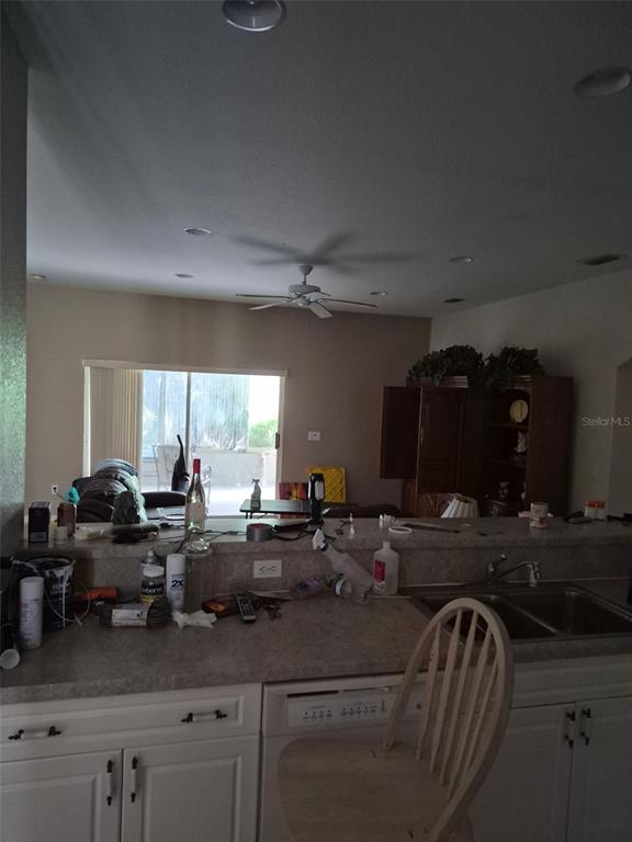 A kitchen with white cabinets and a breakfast bar overlooks a living area with a ceiling fan — 3163 FOREST CREEK DRIVE, MELBOURNE, FL