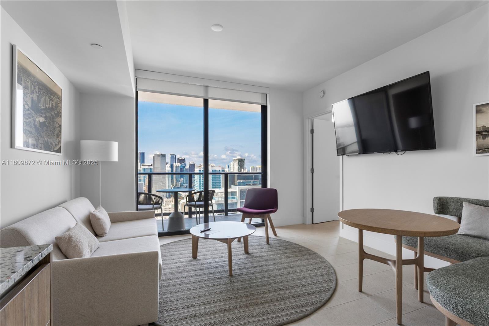 A modern living room features a sofa, round coffee table, dining area, and balcony access — 601 NE 1st St # 3907, Miami FL 33132, MIAMI, FL